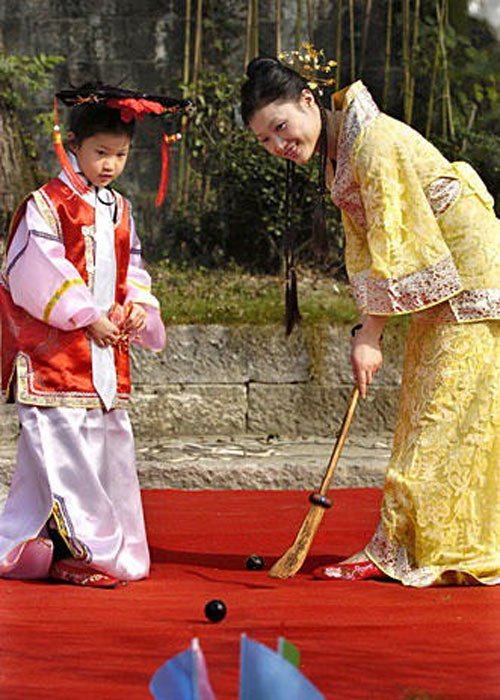 Ein chinesischer Junge und eine Frau in altertümlicher Kleidung spielen Chuiwan-Golf.