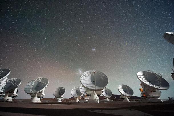 Antennen des Atacama Large Millimeter/submillimeter Array (ALMA), auf dem Chajnantor Plateau in den chilenischen Anden. Die Große und die Kleine Magellansche Wolke, zwei Begleitgalaxien unserer eigenen Milchstraße, sind als helle Flecken am Nachthimmel in der Mitte des Bildes zu sehen.