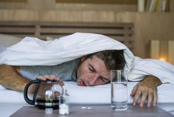 Ein junger, erschöpfter Mann mit einem Kater nach einer durchzechten Nacht. Auch heute noch gibt es verschiedene Katerbehandlungen, von viel Wasser bis hin zu traditionellen Heilmitteln.