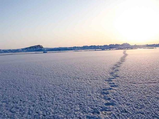 Fußspuren, die über eine verschneite Eismeerlandschaft führen, aber sind die "First Americans" wirklich durch einen Treck über die Beringstraße nach Nordamerika gekommen. Oder kamen sie auf dem Seeweg an? Aktuelle Beweise deuten auf beides hin, aber dass die Seeüberquerung der Landüberquerung um bis zu 20.000 Jahre vorausging.
