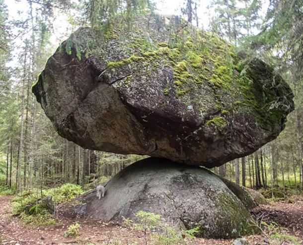 Ein großer Felsbrocken namens Kummakivi („Seltsamer Stein“) in Ruokolahti, Südostfinnland. Ein weißer Zwergschnauzer darunter vermittelt einen Eindruck von der Größe.