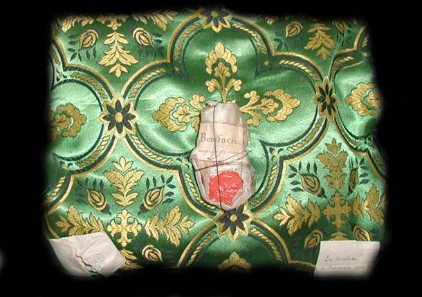 Reliquie aus dem Schrein des Heiligen Bonifatius von Dokkum in der Einsiedlerkirche von Warfhuizen in den Niederlanden. Das Knochenfragment in der Mitte stammt vom Heiligen Bonifatius; die kleinen gefalteten Papiere links und rechts enthalten Knochenfragmente des Heiligen Benedikt von Nursia bzw. Bernhard von Clairvaux. 
